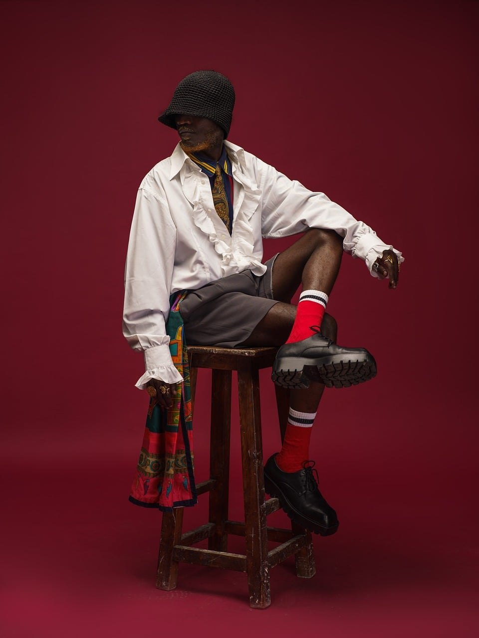 Model in a crisp white shirt seated on a stool against a deep red backdrop, from the FORME STUDIO campaign